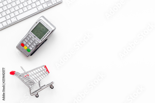 making purchase online with card machine, keyboard and mini trolley on white desk background top view