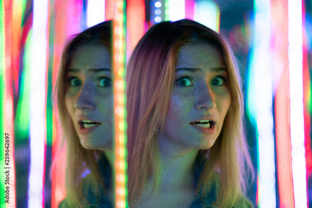 Obraz premium sweet caucasian girl walks in a mirror maze with colorful diodes and enjoys an unusual attraction room in the city
