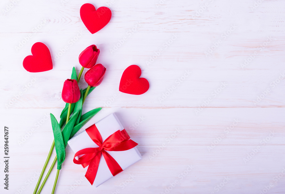Women's day, Mother's day, Valentine's day concept Red tulips bouquet and a gift on white wooden background, top view and copy space for card and advertiser. Women's day, Mother's day, Valentine's day concept Red tulips bouquet and a gift on white wooden background, top view and copy space for card and advertiser.