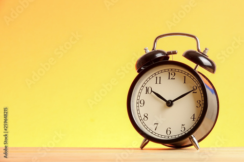 Black alarm clock on the wooden surface against the yellow background.