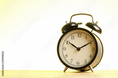 Black alarm clock on the wooden surface against the yellow background.