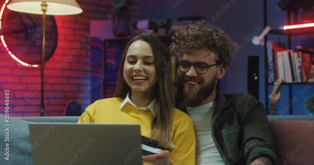 Close up of the cheerful and happy young Caucasian couple having a videochat via web cam on the laptop computer in the evening at home. Close up of the cheerful and happy young Caucasian couple having a videochat via web cam on the laptop computer in the evening at home.