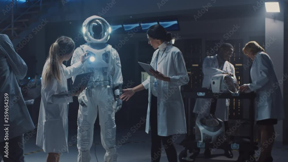 Diverse Team of Aerospace Scientists and Engineers Wearing White Coats have Discussion, Use Computers Design New Space Suit Adapted for Galaxy Exploration and Travel. Constructing Astronaut Suit Diverse Team of Aerospace Scientists and Engineers Wearing White Coats have Discussion, Use Computers Design New Space Suit Adapted for Galaxy Exploration and Travel. Constructing Astronaut Suit