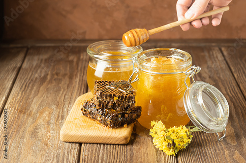 A hand is holding awooden spoon which honey flows. Banks of fresh golden flower honey on a wooden background the table. photo