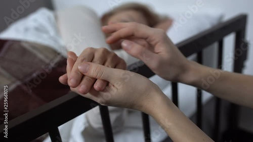 Daughter supporting her terminally ill mother lying on hospital bed, hospice photo