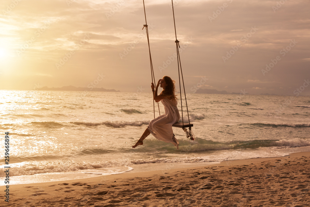 Silhouette of woman on swing above sea shore on sunset