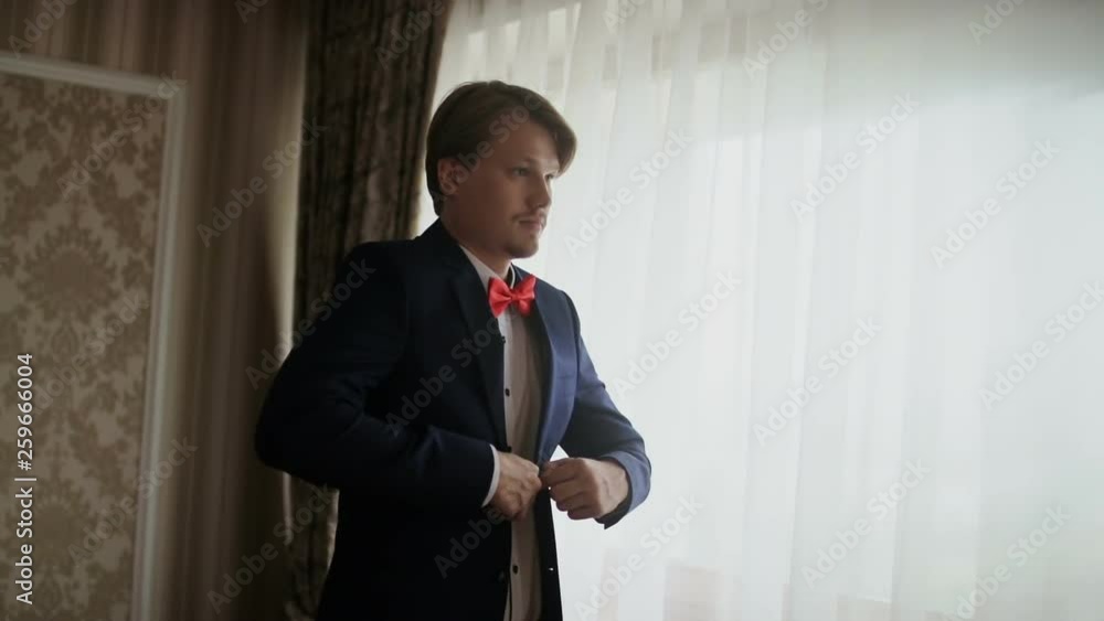 Young man putting on jacket standing by window. Groom is preparing for his wedding in the morning. Young man putting on jacket standing by window. Groom is preparing for his wedding in the morning.