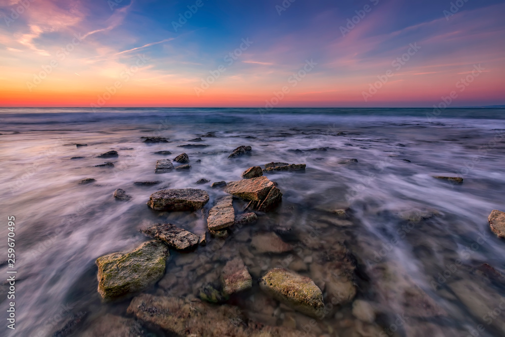 Obraz premium Beautiful rocky beach with stones in blurred water, the colorful sky at sunrise. Black sea, Bulgaria. Landscape with the sea waves and rocks.