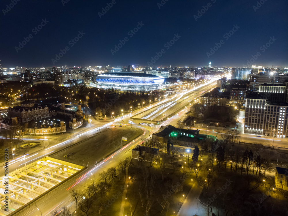 Night cityscape of soccer stadium and highway with trails of cars captured with long exposure. UAV drone aerial view
