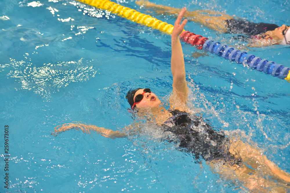 Young girl in goggles and cap swimming in the blue water pool