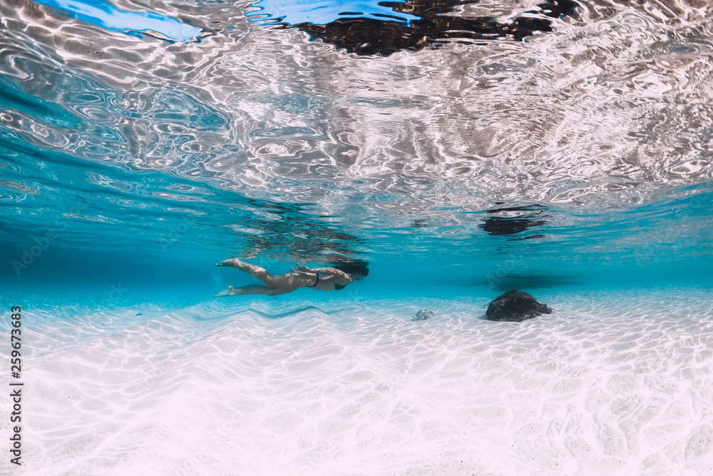 Young woman swimming underwater in the tropical blue ocean with white sand