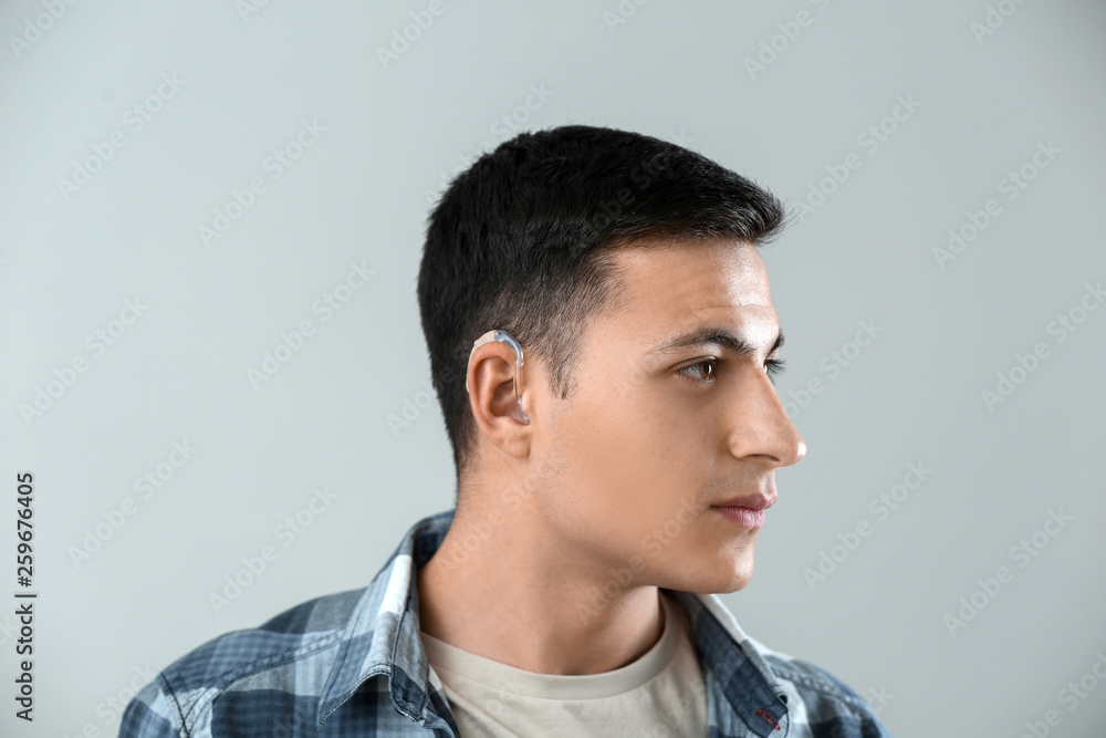 Young man with hearing aid on grey background Young man with hearing aid on grey background