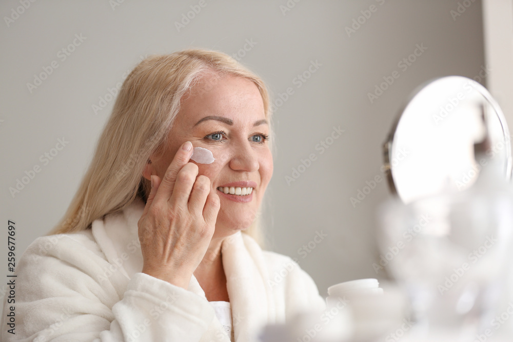 Mature woman applying facial cream at home
