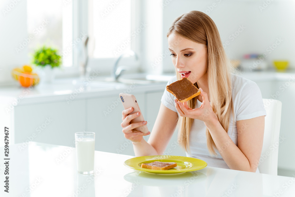 Portrait of her she nice-looking cute charming attractive cheerful straight-haired girl wearing white tshirt having good beverage snack lunch typing sms in light white interior room Portrait of her she nice-looking cute charming attractive cheerful straight-haired girl wearing white tshirt having good beverage snack lunch typing sms in light white interior room
