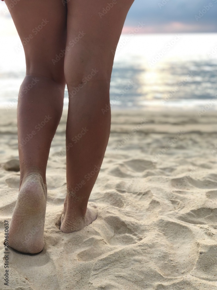 sexy women's tanned legs in the white fine sand of the unique Karon beach of Phuket on the background of the sea and the Golden sunset, a sense of pleasure and harmony sexy women's tanned legs in the white fine sand of the unique Karon beach of Phuket on the background of the sea and the Golden sunset, a sense of pleasure and harmony