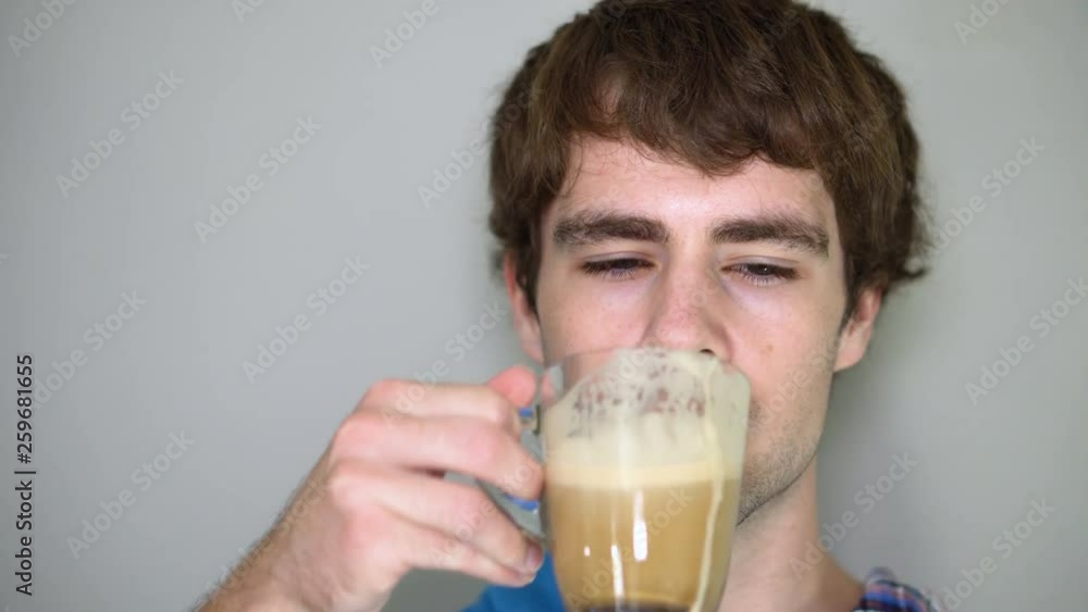 Face of 20s Caucasian Man Drinking Caffe Latte From Glass Cup With Gray Background Face of 20s Caucasian Man Drinking Caffe Latte From Glass Cup With Gray Background