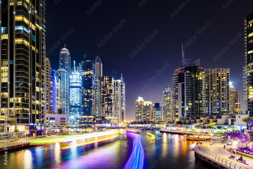 Naklejka premium Stunning view of the Dubai Marina at dusk with illuminated skyscrapers in the background and a light trails left by a yacht sailing in the foreground. Dubai, United Arab, Emirates.