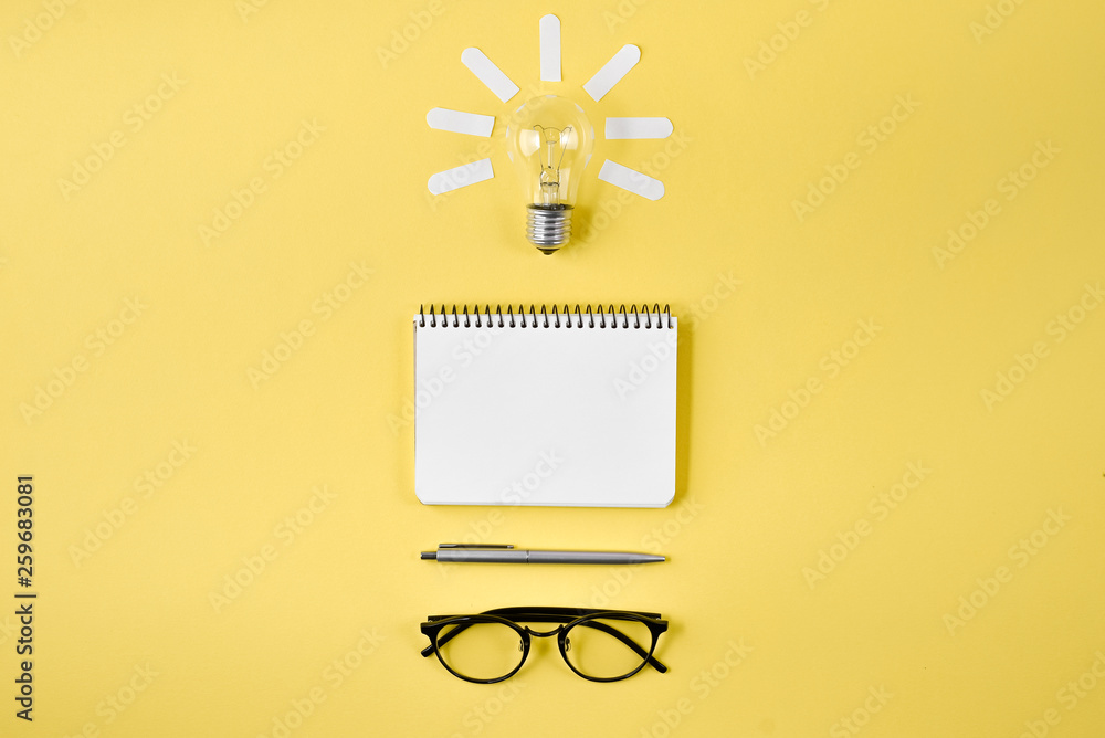 Financial planning table top with pen, notepad, eyeglasses and light bulb on yellow background. Concept brainstorming and new idea - obrazy, fototapety, plakaty 