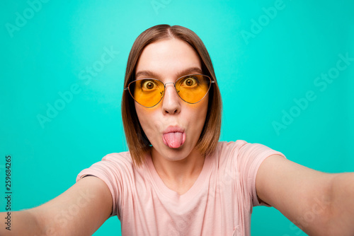 Close up photo beautiful her she lady modern look short straight hair make take selfies instagram post followers tongue out mouth careless wear specs casual t-shirt isolated teal turquoise background