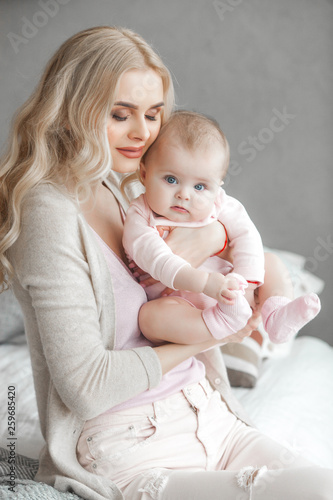 Young mother with her little cute baby daughter. Little baby girl and her mom. Mama with her child indoor.