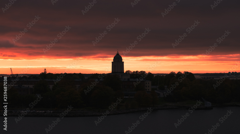 Scenic city slhouette with red sunset and dark mood at spring evening in Helsinki, Finland. Suomenlinna tower silhouette.