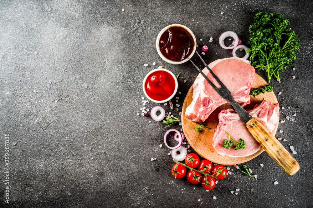 Raw meat, pork steaks, ready for cooking, with herbs, black concrete background copy space