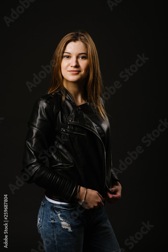 Young caucasian woman wearing a leather jacket and jeans posing on the black background