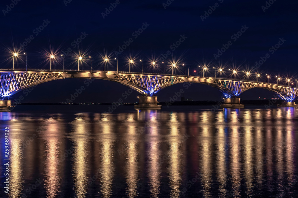 a fragment of an automobile bridge across the Volga River at night lit by lanterns, Saratov Russia