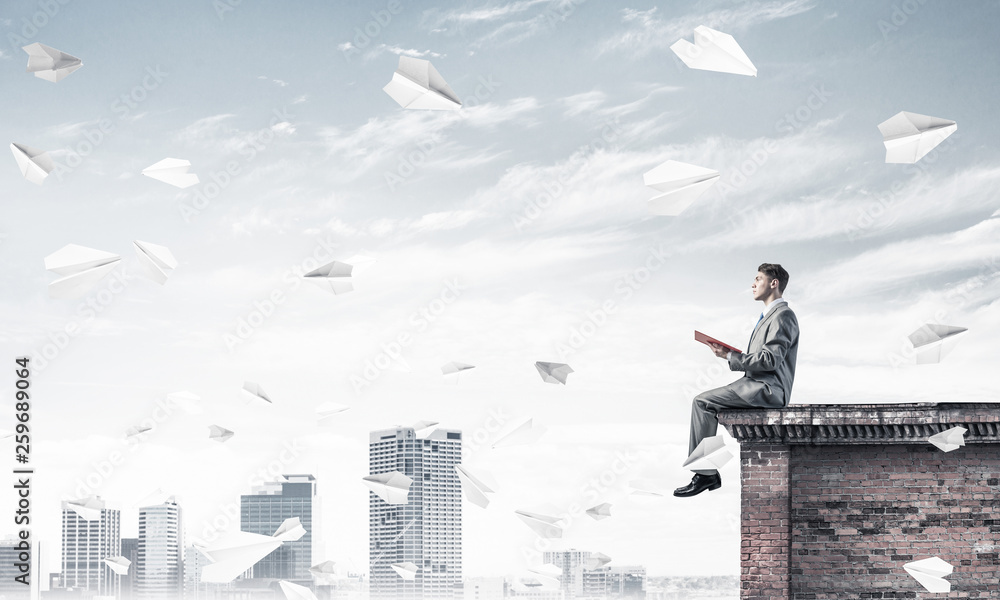 Man on roof edge reading book and cityscape at background Man on roof edge reading book and cityscape at background