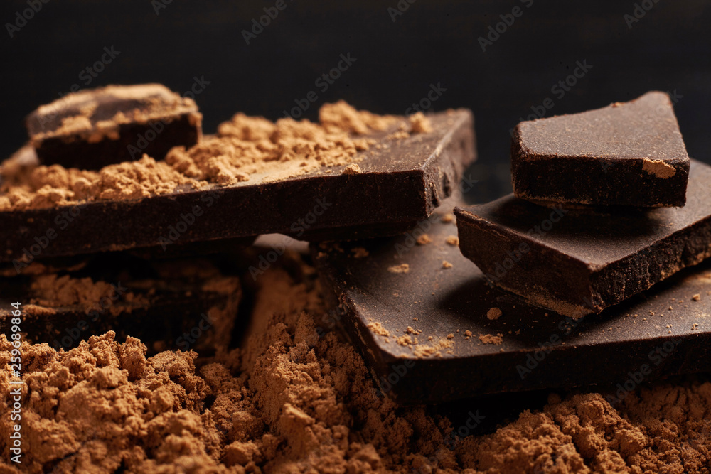Broken dark chocolate and cocoa on black background. Broken dark chocolate and cocoa on black background.
