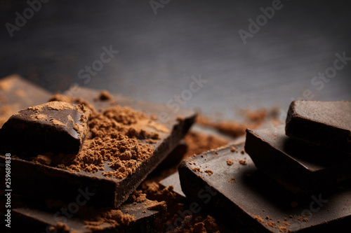 A pieces of dark chocolate and cocoa on black baackground..