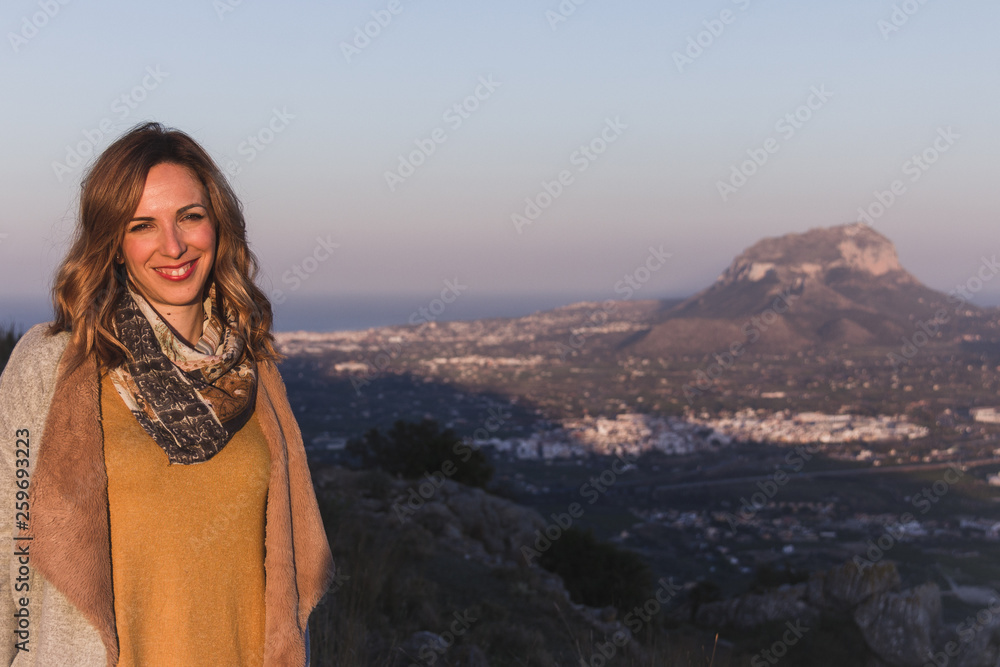 Portrait of a young woman with ochre colored clothes, posing in a beautiful landscape at sunset. Montgo mountain is in the background, in Spain