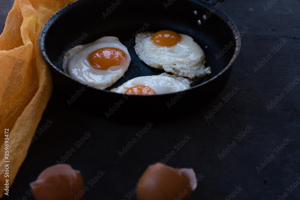 Overhead view of  fried eggs in black baking pan on dark background