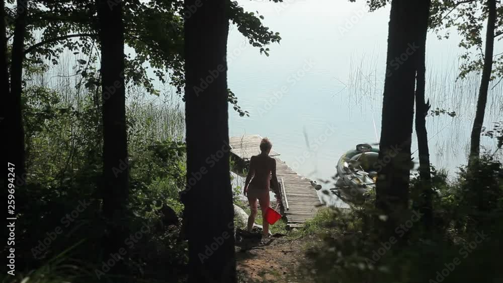 A woman in a swimsuit with a bucket in her hands is on a wooden pier. A woman in a swimsuit with a bucket in her hands is on a wooden pier.