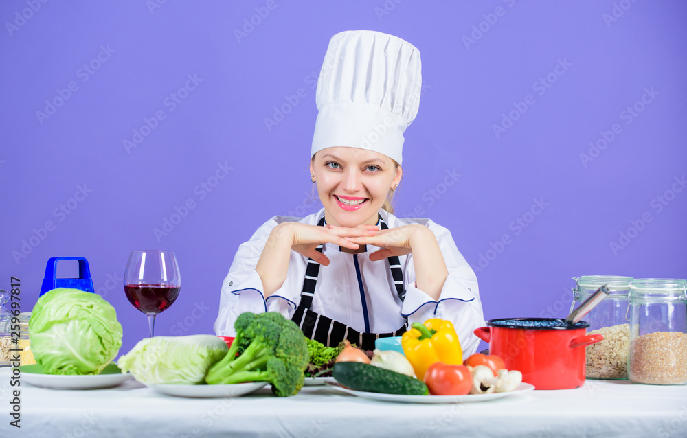 Kitchen inspiration. Adorable kitchen maid. Pretty chef smiling with organic natural food on kitchen table. Happy cook sitting on show kitchen in restaurant Kitchen inspiration. Adorable kitchen maid. Pretty chef smiling with organic natural food on kitchen table. Happy cook sitting on show kitchen in restaurant