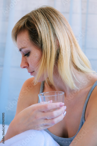 beautiful blonde girl sitting in bed just waking up drinking a morning glass of water. Blonde freckled fresh morning.