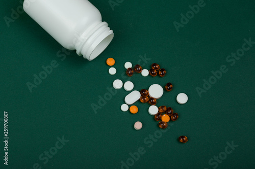 Medicine concept - colorful pills and white medical bottle on green paper background