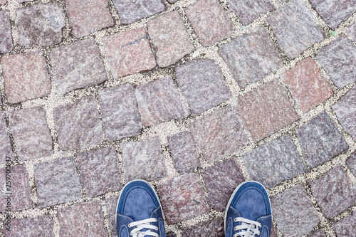 Man feet in blue jeans sneakers on cobbled road