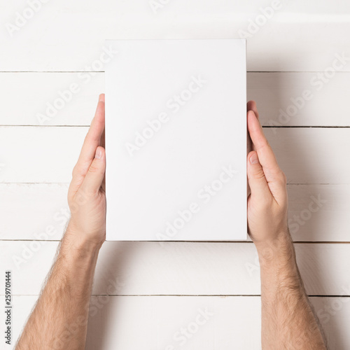 White rectangular box in male hands. Top view. White table on the background