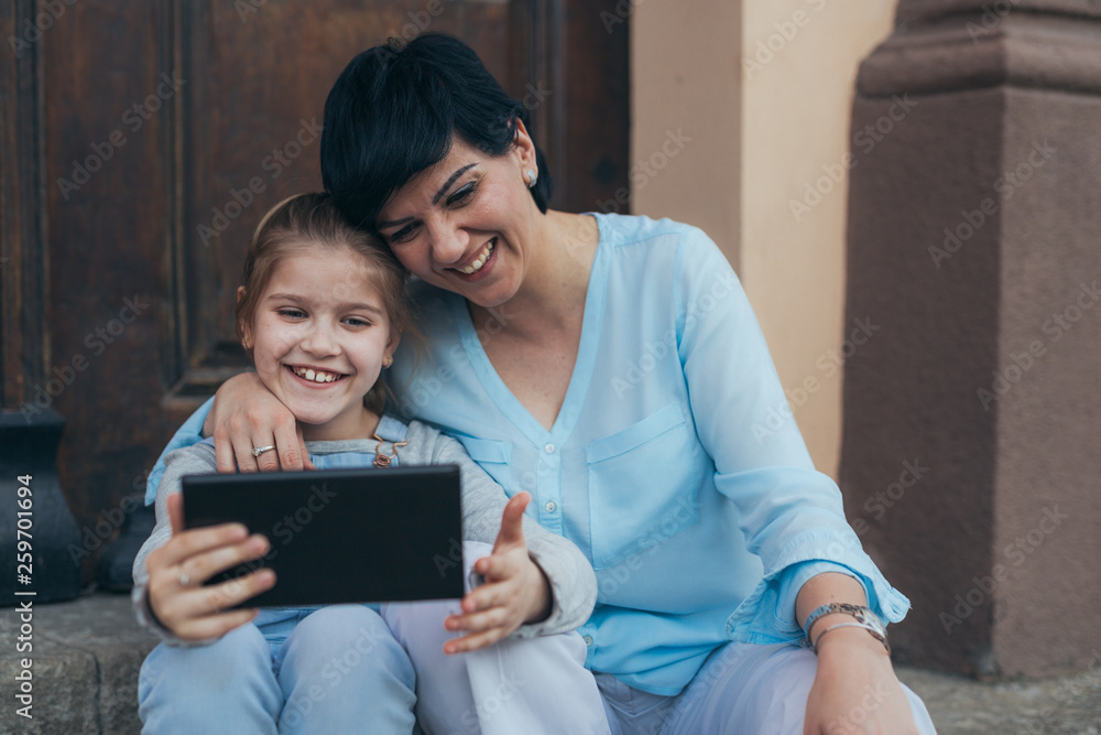 girl using laptop with her mother, sitting on stairs outdoor in the city girl using laptop with her mother, sitting on stairs outdoor in the city