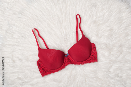 Red bra with lace on white fur. Flat lay. Fashion lingerie concept.
