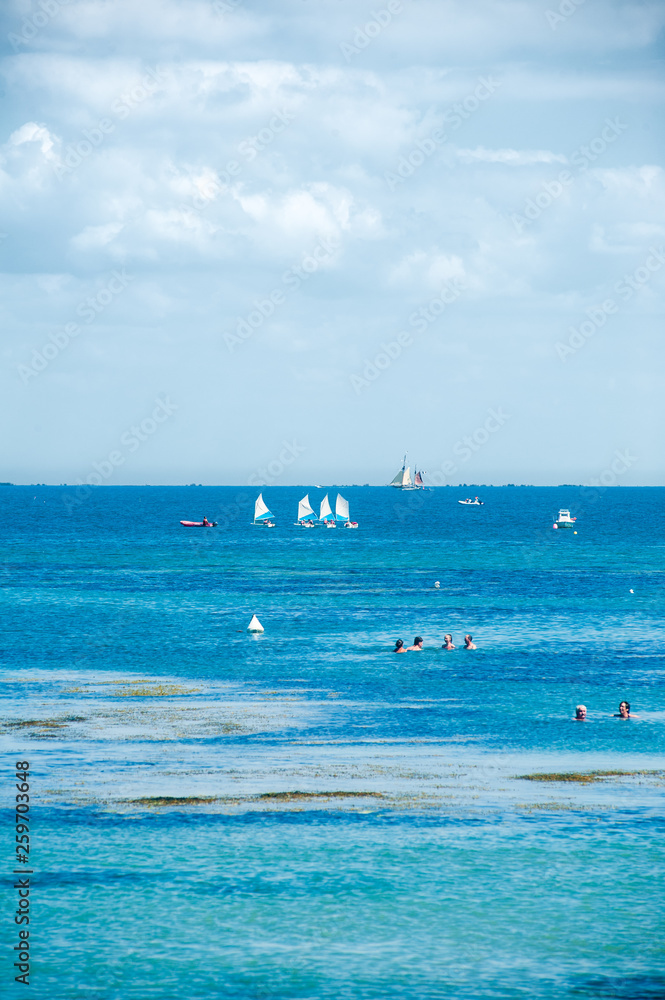 people swimming in the sea in summertime on the isle of Noirmoutier with some boats in the background
