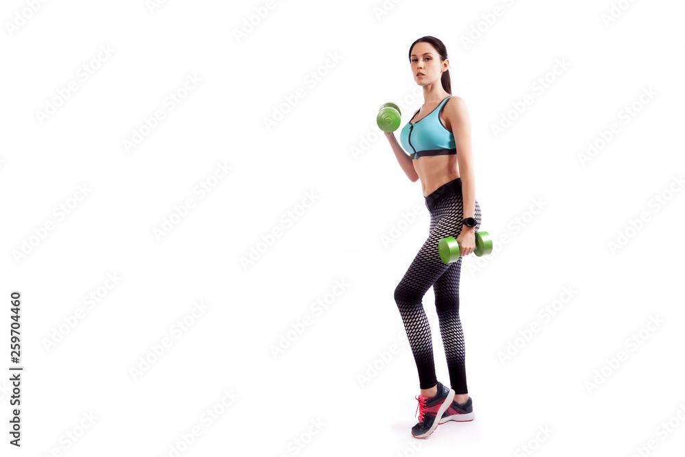 Young sportive woman fitness model brunette doing exercise with dumbbell on biceps on white isolated background. Fit girl living an active lifestyle Young sportive woman fitness model brunette doing exercise with dumbbell on biceps on white isolated background. Fit girl living an active lifestyle