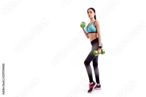 Young sportive woman fitness model brunette doing exercise with dumbbell on biceps on white isolated background. Fit girl living an active lifestyle