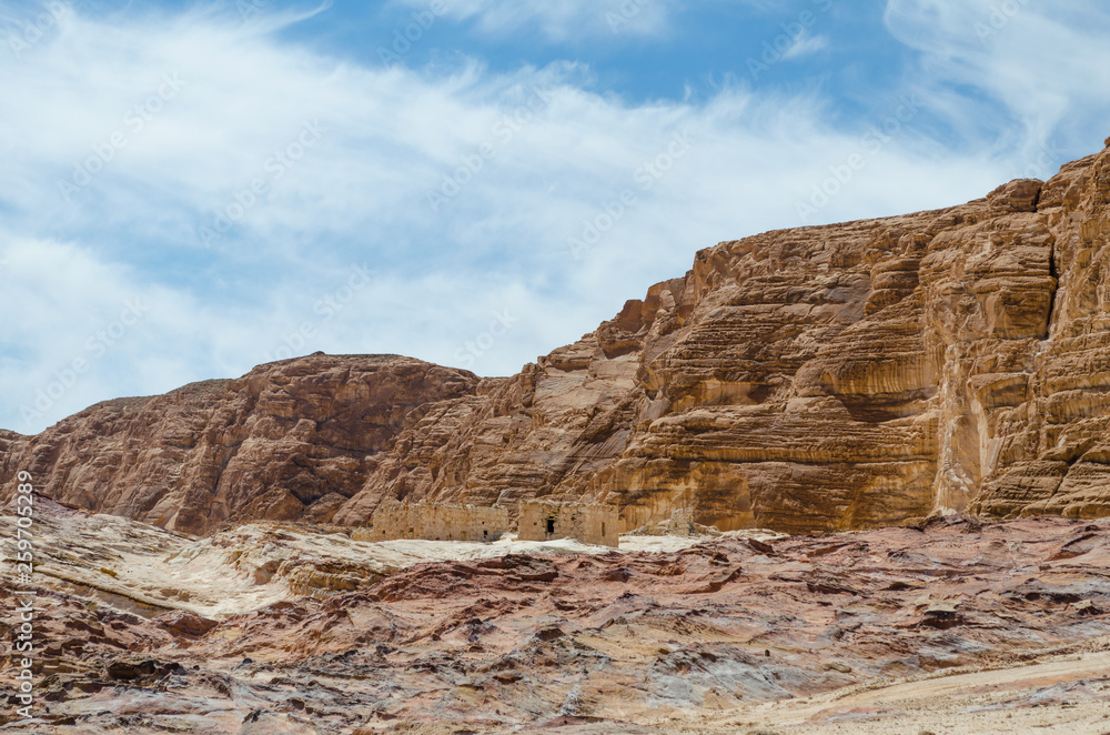 Fototapeta premium ruins of houses in the desert against the backdrop of high rocky mountains and blue sky with white clouds in Egypt Dahab South Sinai