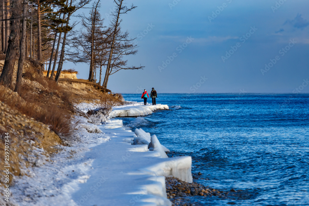 Two people walking on the shore of Baikal lake in winter