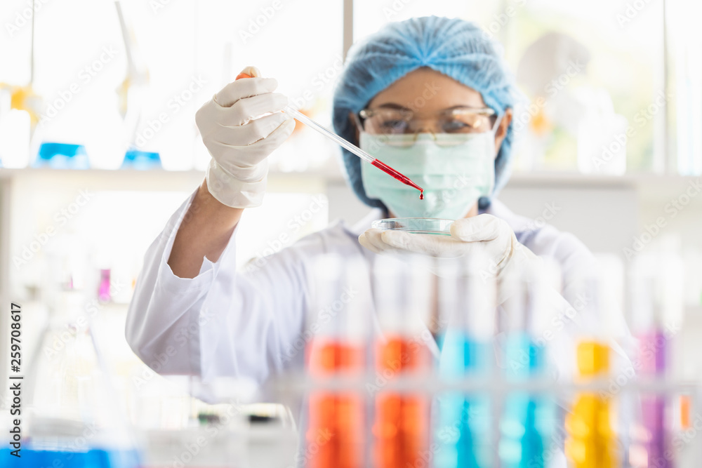 Female scientist dropping red liquid into beaker.. Female scientist dropping red liquid into beaker..
