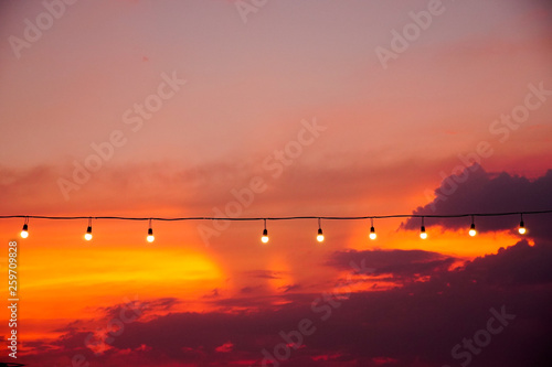 vintage light bulbs on string wire against sunset.