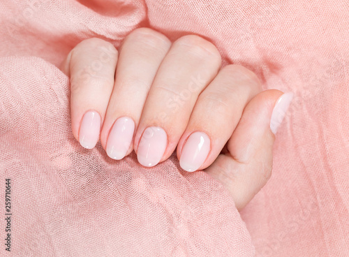 Top view closeup photography of beautiful female hands isolated on soft pink elegant fabric texture background. Fingernails with fresh professional light pink color manicure.