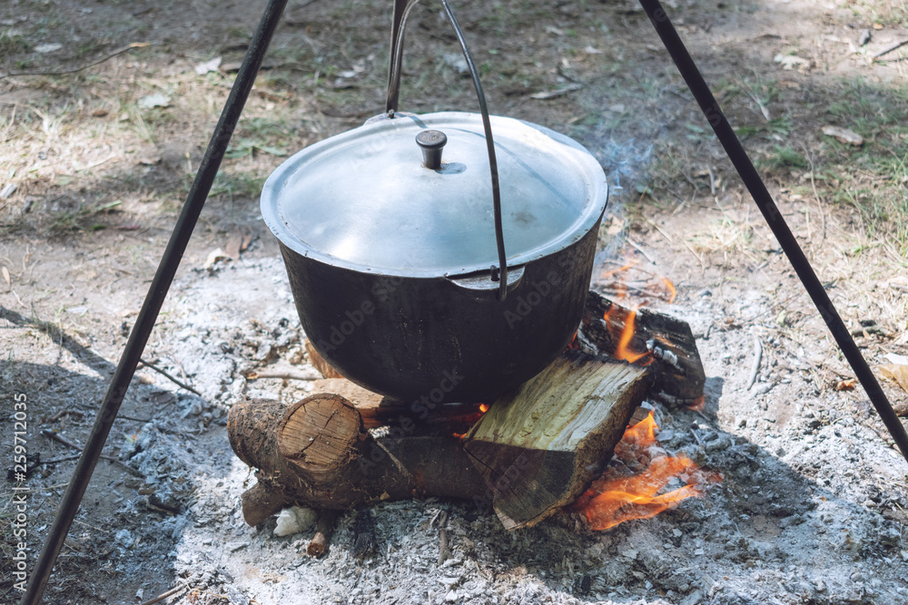 Hiking pot, Bowler in the bonfire. Fish soup boils in cauldron at the stake. Traveling, tourism, picnic cooking Hiking pot, Bowler in the bonfire. Fish soup boils in cauldron at the stake. Traveling, tourism, picnic cooking